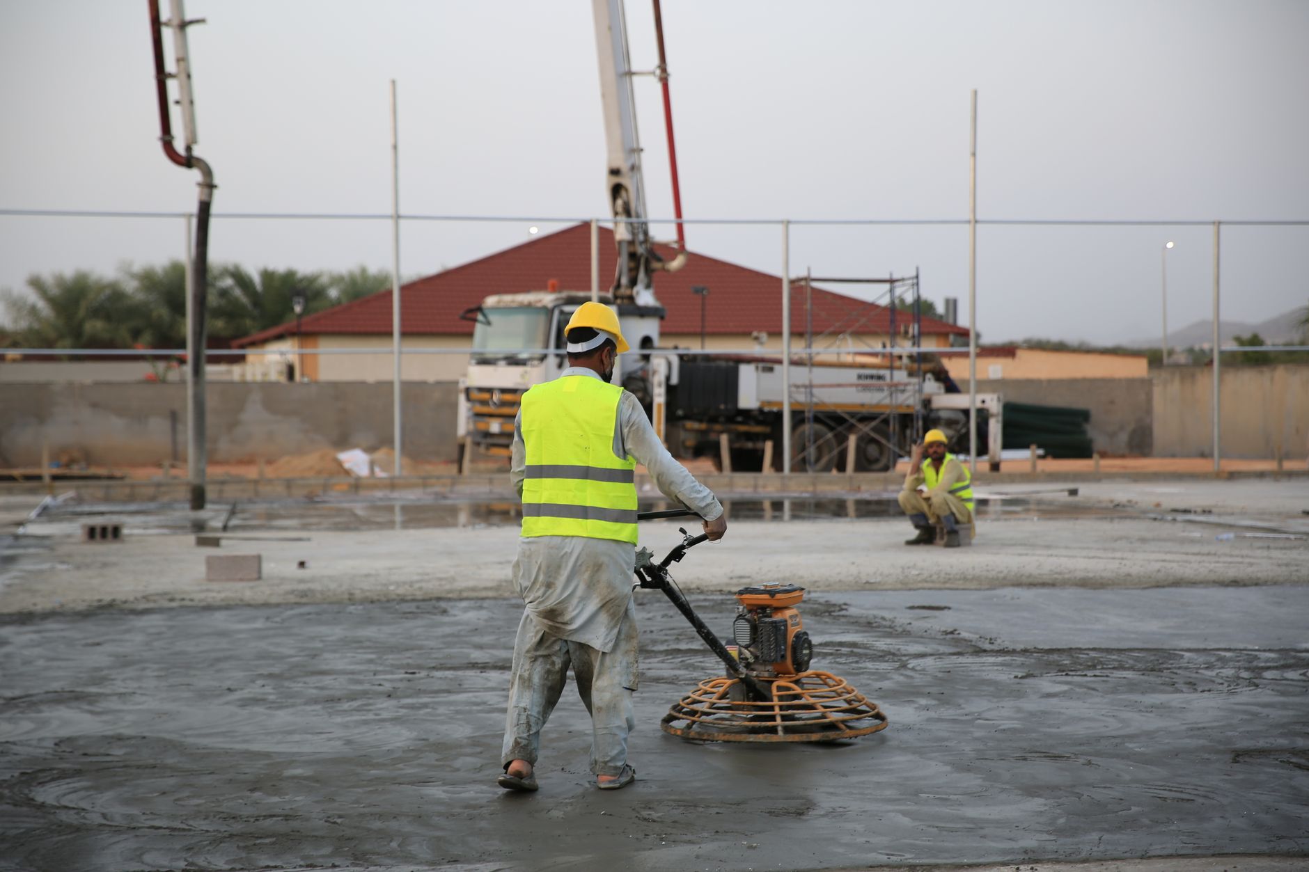 Workers smoothing concrete on a construction site with heavy machinery equipment in Carlsbad, CA